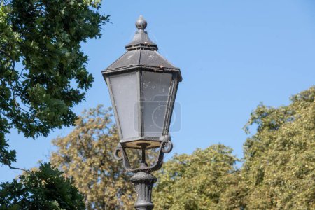 Téléchargez les photos : Un gros plan d'une lanterne sale capturée à la lumière du jour contre un ciel bleu et des arbres feuillus - en image libre de droit