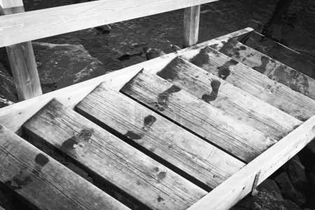 Téléchargez les photos : Un plan en niveaux de gris des pas humides sur l'escalier en bois au-dessus de l'eau du lac - en image libre de droit