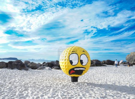 Téléchargez les photos : Une grande balle de golf jaune avec un visage sur la plage pendant le Swell Sculpture Festival - en image libre de droit