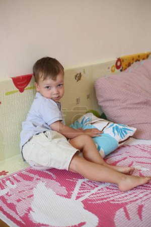Photo for A Caucasian cute boy kid playing with pillows on bed at home - Royalty Free Image