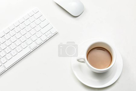 Foto de Una taza de café blanco junto a un teclado y el ratón de la computadora - Imagen libre de derechos