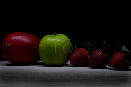 Téléchargez les photos : Un gros plan de deux pommes et trois fraises sur fond sombre - en image libre de droit