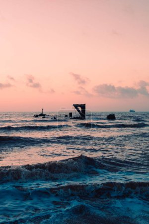 Foto de Una vertical de partes de un viejo muelle destrozado en el mar ondulado bajo el hermoso cielo - Imagen libre de derechos