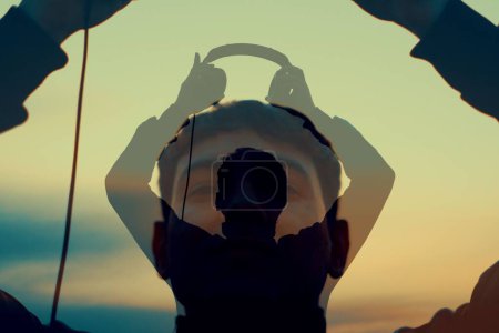 Téléchargez les photos : La silhouette d'un jeune homme portant le casque avec ses projections au coucher du soleil - en image libre de droit
