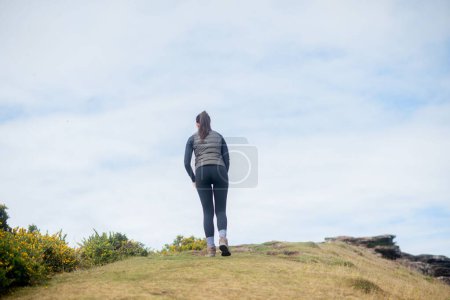 Foto de Una vista trasera de una hembra caminando sobre una colina contra el cielo nublado - Imagen libre de derechos