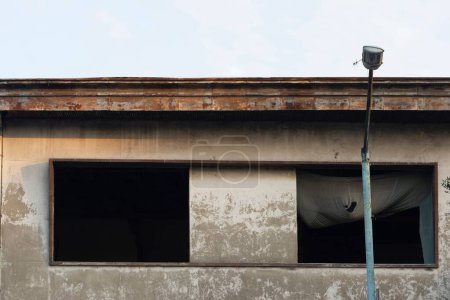 Foto de Una linterna de calle con un viejo edificio abandonado con una azotea oxidada en el fondo durante el día - Imagen libre de derechos