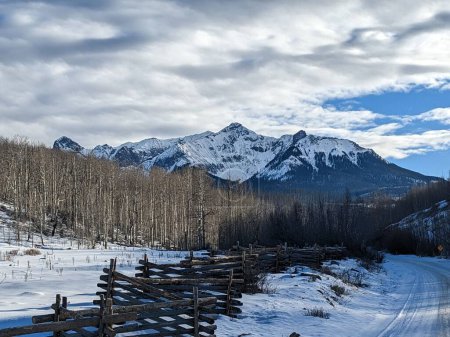 Foto de La vista de un camino rural cubierto de nieve con una valla en el fondo de las montañas. - Imagen libre de derechos