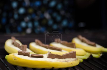 Téléchargez les photos : Gros plan d'une banane tranchée ouverte et décorée de petits cubes de chocolat - en image libre de droit