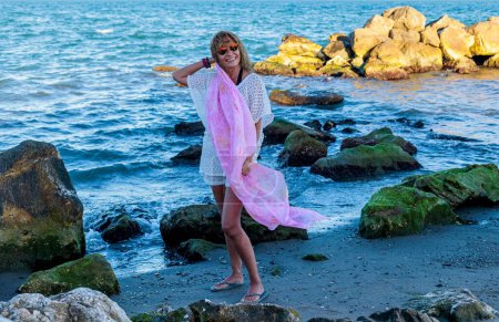 Photo for A Hispanic female model over 50 years with pink scarf and sunglasses on the beach - Royalty Free Image