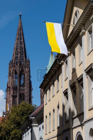 Foto de Un disparo vertical de la catedral de Freiburger Munster y la bandera de la iglesia católica en Alemania. - Imagen libre de derechos