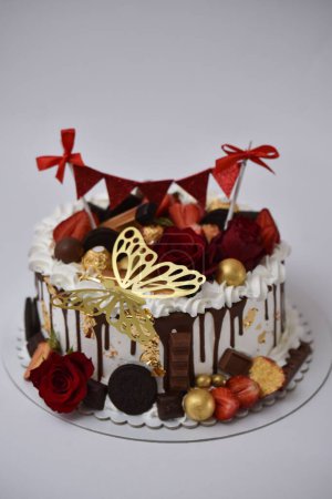 Foto de Un primer plano vertical de un pastel decorado con una mariposa dorada, barras de chocolate y flores - Imagen libre de derechos