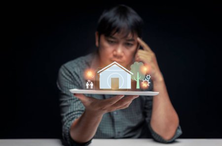 Téléchargez les photos : Un jeune Asiatique du Sud-Est tenant une tablette avec une maison rendue en 3D - premier concept d'achat d'une maison - en image libre de droit