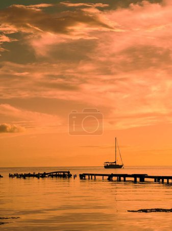 Téléchargez les photos : Une silhouette d'un yacht naviguant dans une mer et une ancienne jetée en bois au coucher du soleil - en image libre de droit