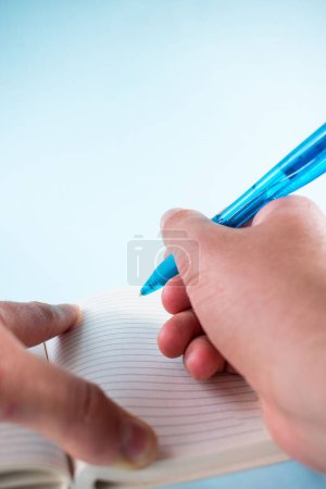 Foto de Una mano sosteniendo un bolígrafo azul y escribiendo sobre el papel sobre un fondo blanco - Imagen libre de derechos