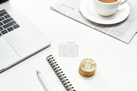 Foto de Una vista superior de una mesa de oficina blanca con un cuaderno, monedas de oro y una taza de café - Imagen libre de derechos
