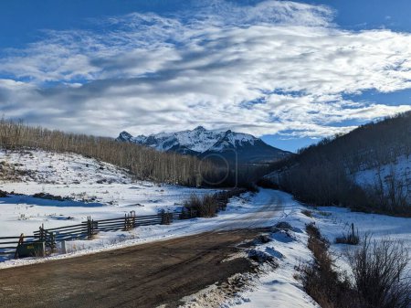 Téléchargez les photos : La vue d'une route rurale enneigée avec des montagnes en arrière-plan. - en image libre de droit
