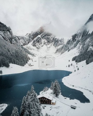 Foto de Un plano vertical de un lago rodeado de colinas rocosas cubiertas de nieve en invierno en Suiza - Imagen libre de derechos