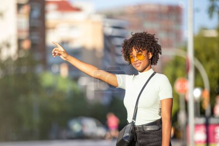 Foto de Una hermosa joven afro-peluda parada en la calle y tomando un taxi con la mano en alto - Imagen libre de derechos