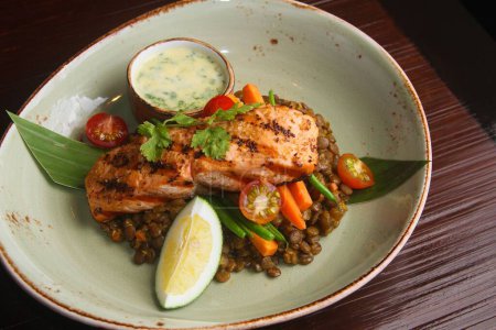 Téléchargez les photos : Un gros plan de délicieux plat de saumon rôti et de lentilles à côté d'une sauce dans un restaurant - en image libre de droit