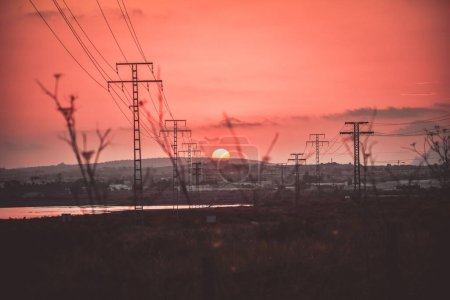 Foto de Una vista panorámica de las torres de energía y líneas en un campo durante la puesta del sol - Imagen libre de derechos