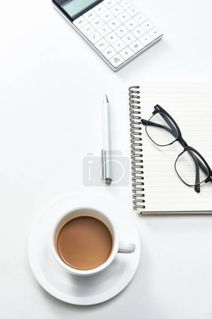 Photo for A vertical top view of a white office table with a notebook, glasses and a cup of coffee - Royalty Free Image