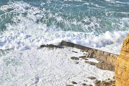 Téléchargez les photos : Un plan aérien envoûtant de vagues mousseuses orageuses qui s'écrasent contre un rivage rocheux - en image libre de droit