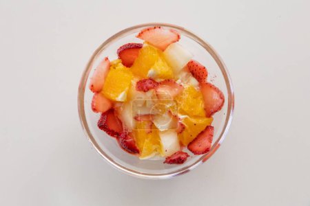 Foto de Un primer plano de vista superior de un tazón de fruta con fresas frescas y rodajas de naranja en una superficie blanca - Imagen libre de derechos