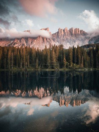Foto de Un plano vertical de un lago rodeado por un bosque y dolomitas italianas durante el amanecer - Imagen libre de derechos