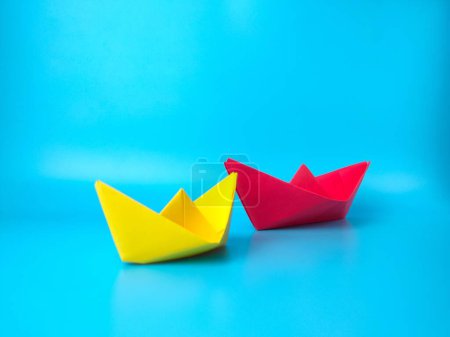 Foto de Una gran nave de papel rojo y una más pequeña amarilla sobre fondo turquesa - concepto de liderazgo - Imagen libre de derechos