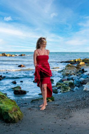 Téléchargez les photos : Une verticale d'une femme hispanique en robe rouge courant sur la plage - en image libre de droit