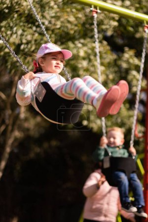 Téléchargez les photos : Une caucasienne fille balançant dans aire de jeux - en image libre de droit