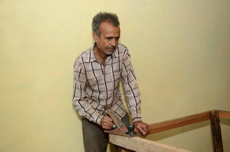 Téléchargez les photos : Un vieil homme indien travaillant dans un atelier de bois avec un avion - en image libre de droit