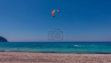 Téléchargez les photos : Un kiteboarder tiré par un cerf-volant de puissance à travers la mer sur un fond bleu ciel - en image libre de droit