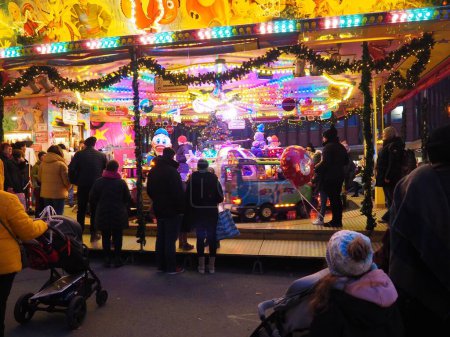 Téléchargez les photos : Les gens dans un beau parc de Noël avec des décorations de dessins animés et des enfants chevauchant un carrousel drôle - en image libre de droit