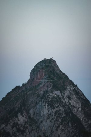 Photo for A vertical shot of a mountain peak and green trees at the slope at sunset - Royalty Free Image