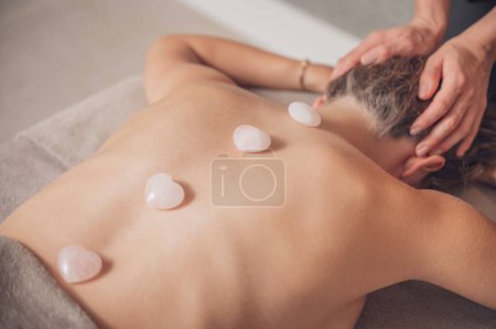 Photo for A woman during spa massage procedure with white stones on her back - Royalty Free Image