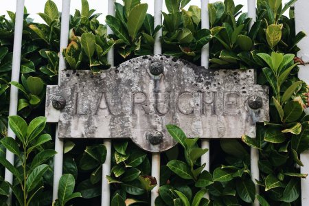 Téléchargez les photos : Une clôture métallique avec grand arbuste de laurier aux feuilles vertes et panneau "LARUCHE" - en image libre de droit