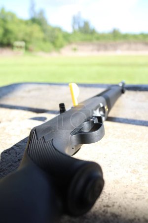 Téléchargez les photos : Un gros plan d'un pistolet noir avec un long canon pointant sur les champs d'herbe ensoleillés - en image libre de droit