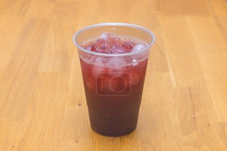 Foto de Un vaso de plástico lleno de limonada de cerezo con hielo puesto en la mesa de madera - Imagen libre de derechos
