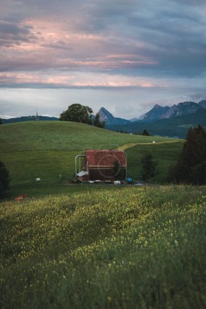 Foto de Un plano vertical de casa de campo en campo verde con montañas y cielo nublado en el fondo - Imagen libre de derechos