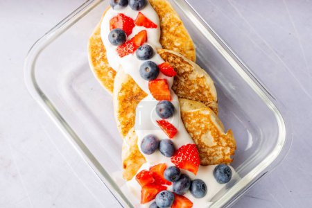 Photo for A top view of healthy pancakes topped with yogurt and berries in the glass container - Royalty Free Image