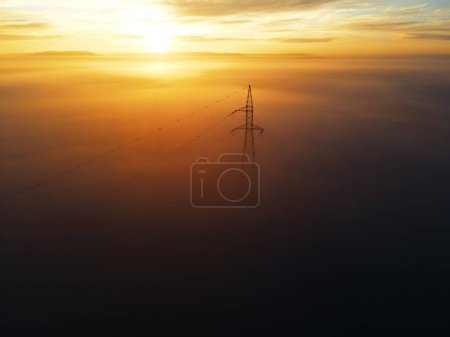 Téléchargez les photos : Une scène orange coucher de soleil avec une tour de transmission dans le brouillard - en image libre de droit