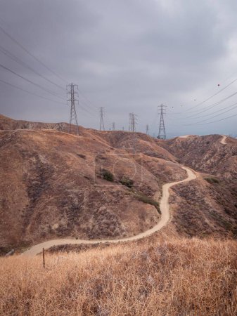 Foto de Un camino de tierra solitario serpentea alrededor de una montaña con torres de telefonía celular en la distancia - Imagen libre de derechos