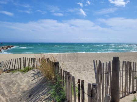 Foto de Una cerca de madera en la playa vacía con el mar detrás de ella bajo el cielo azul nublado - Imagen libre de derechos