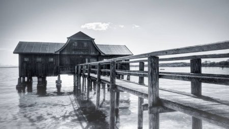 A black and white view of a boathouse at the Ammersee lake with a jetty next to it in Germany