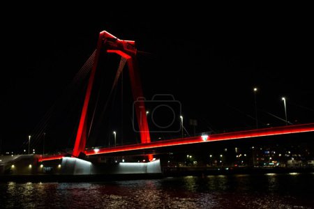 Téléchargez les photos : Paysage urbain nocturne avec pont en acier en rouge vif dans le paysage urbain de Rotterdam vu de dessous sur la rivière Maa - en image libre de droit