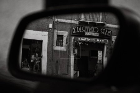 Téléchargez les photos : Une échelle de gris de l'entrée d'un bar reflétée dans le rétroviseur d'une voiture - en image libre de droit