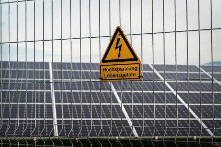 Téléchargez les photos : Une clôture sur le fond des panneaux solaires avec un signe allemand : haute tension, danger pour la vie - en image libre de droit