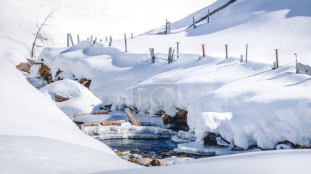 Foto de Una vista panorámica de las montañas alpinas cubiertas de nieve con un arroyo que fluye a través de la nieve - Imagen libre de derechos
