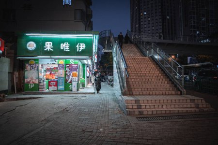 Foto de Una mujer caminando al lado de la tienda y el hombre bajando desde el puente peatonal por la noche en el distrito de Tang Qiao, Shanghai, China - Imagen libre de derechos
